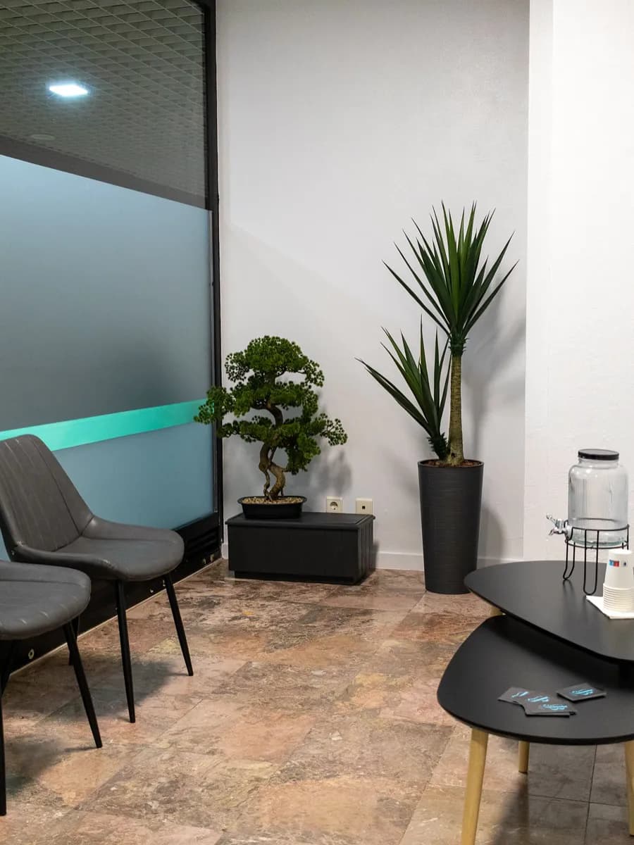 Sala de espera com cadeiras cinzentas, plantas e mesa de apoio